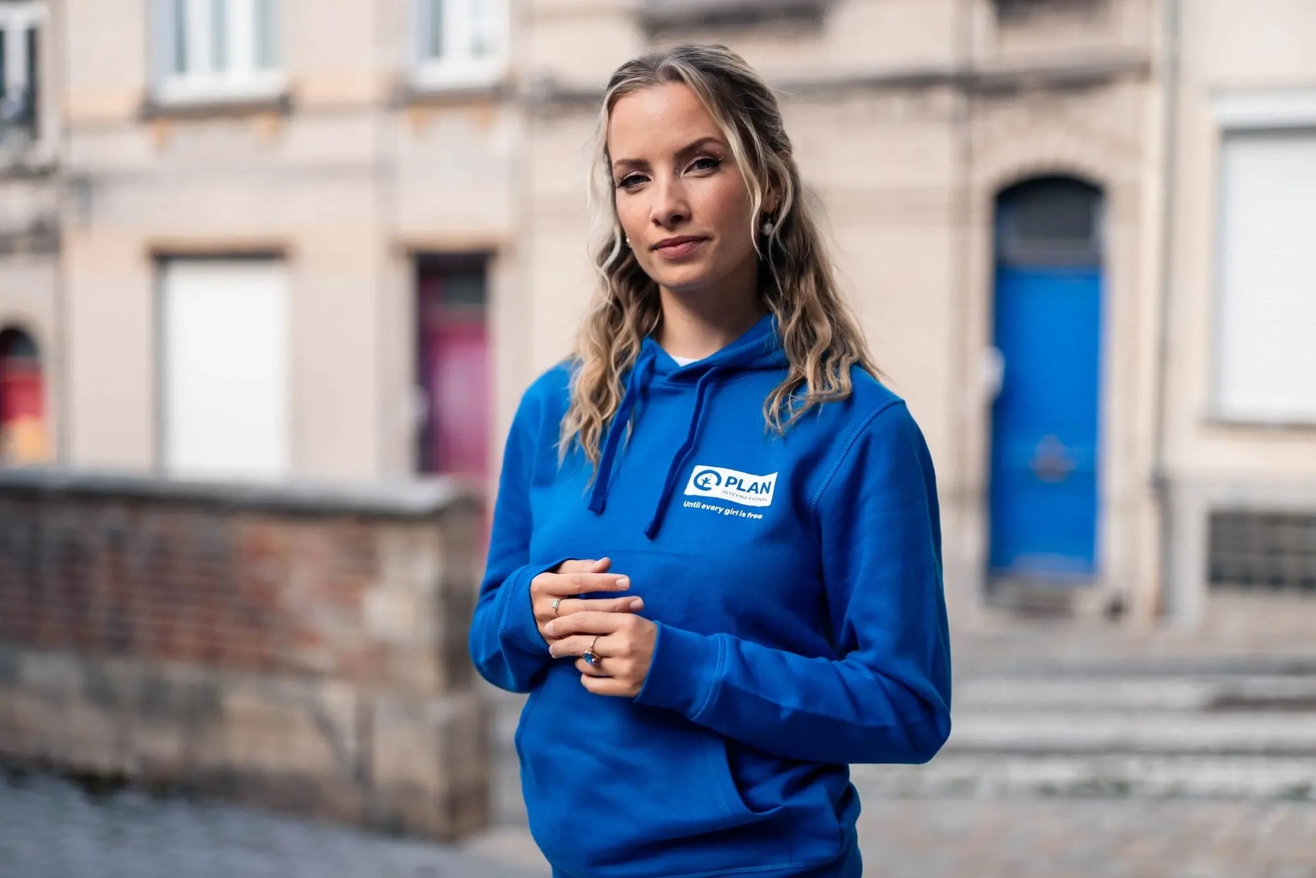 Olivia Trappeniers poseert op straat met een blauwe hoodie van Plan International België